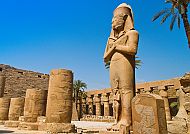 Statue im Karnak-Tempel vor blauem Himmel und Palmen.