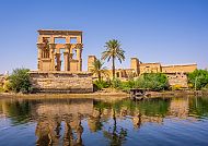 Philae-Tempel am Wasser, sonnig und friedlich, mit Palmen.