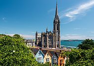 St. Colman's Cathedral in Cobh, bunte Häuser und blauer Himmel.