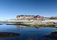 Rote Häuser in Ilulissat vor klarem Himmel und ruhigem Wasser.