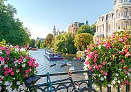 Amsterdam, Blühende Brücke über Amsterdams Kanal mit Fahrrad und Booten., Amsterdam-Kanal mit Blumen und Fahrrad, idyllische Stadtszene.