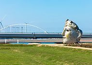 Nijmegen, Kunstwerk in Nijmegen mit Brücke im Hintergrund bei klarem Himmel.