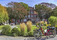 Büsum-Rathauspark-Fahrrad, Fahrrad im idyllischen Büsum-Rathauspark vor historischem Gebäude., Fahrrad im idyllischen Rathauspark von Büsum.