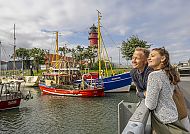 Hafenspaziergang B?sum, Paar genießt den Blick auf den Hafen von Büsum mit Leuchtturm.