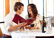 Paar lacht beim Abendessen im Restaurant mit Wein und Menü.