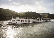 A-ROSA AQUA auf malerischer Flussfahrt vor grüner Hügellandschaft.